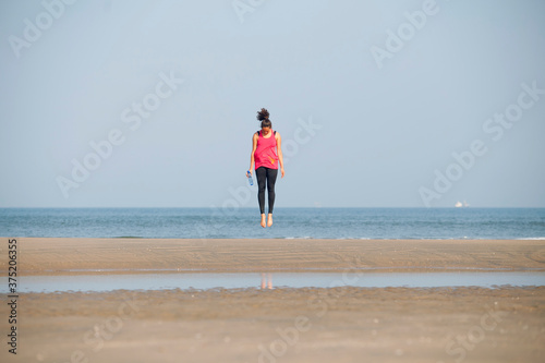 Healthy young woman jumping on the beach during her workout.