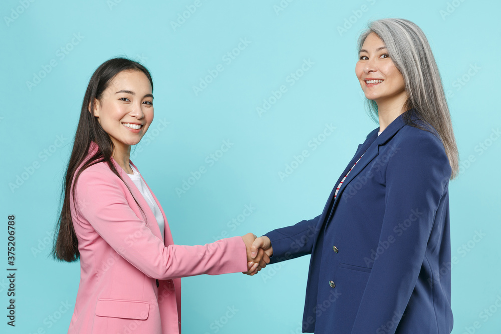Side view of smiling asian female business women employer employee in pink blue jackets working in office tanding with outstretched hand for greeting isolated on blue color background studio portrait. Side view of smiling asian female business women employer employee in pink blue jackets working in office tanding with outstretched hand for greeting isolated on blue color background studio portrait.