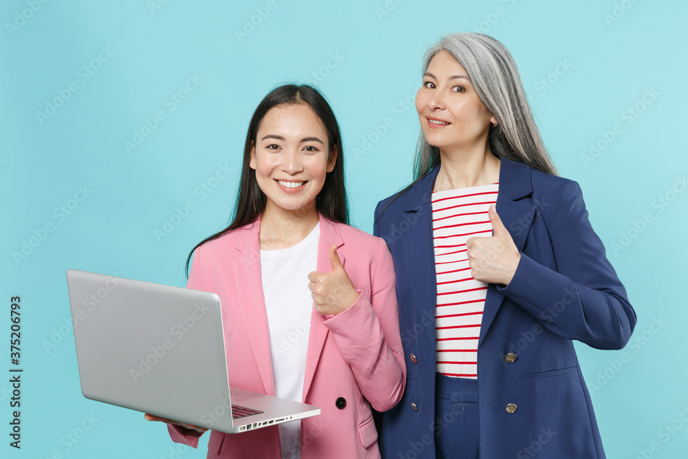 Smiling two asian female business women employer and employee in pink blue jackets working in office using laptop pc computer showing thumb up isolated on pastel blue color background studio portrait. Smiling two asian female business women employer and employee in pink blue jackets working in office using laptop pc computer showing thumb up isolated on pastel blue color background studio portrait.