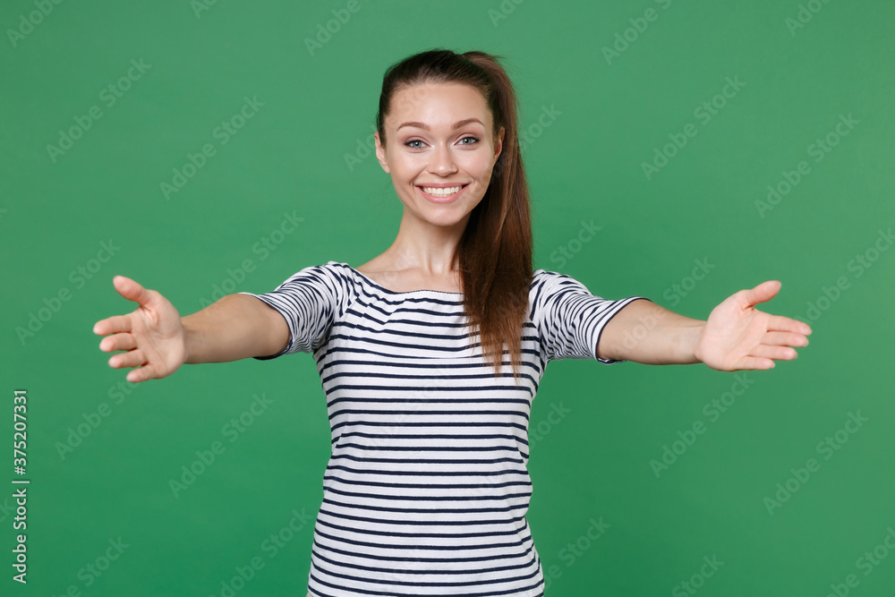 Smiling joyful attractive young brunette woman 20s wearing striped casual clothes posing standing reach out stretch hands looking camera isolated on green color wall background, studio portrait. Smiling joyful attractive young brunette woman 20s wearing striped casual clothes posing standing reach out stretch hands looking camera isolated on green color wall background, studio portrait.