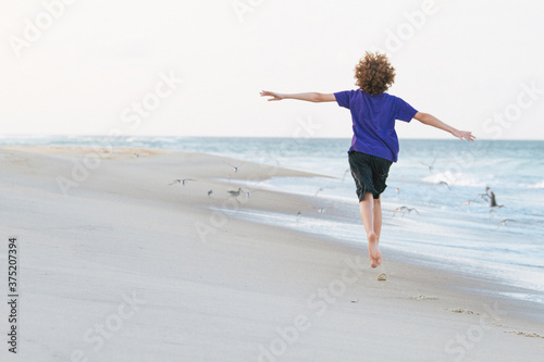 Young white boy with red curly hair running on beach photo