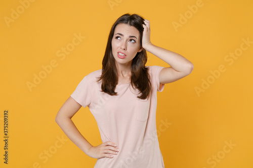 Preoccupied puzzled pensive young brunette woman wearing pastel pink casual t-shirt standing posing put hand on head looking aside up isolated on bright yellow color wall background studio portrait.