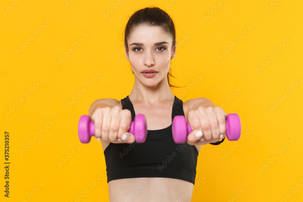 Beautiful young fitness sporty woman 20s wearing black sportswear posing training working out doing exercise with dumbbells looking camera isolated on yellow color wall background studio portrait. Beautiful young fitness sporty woman 20s wearing black sportswear posing training working out doing exercise with dumbbells looking camera isolated on yellow color wall background studio portrait.