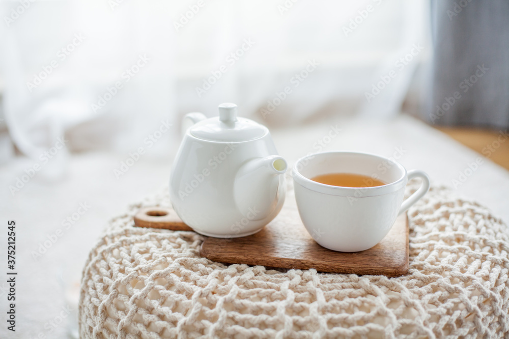 A mug of hot tea, a teapot, a wooden stand on an ottoman. Cozy autumn. Winter breakfast. Cotton.