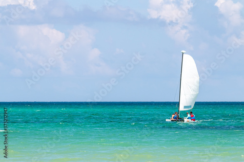 Nautical background of a white sailboat in bright sunlight, on blue ocean water, with space for text