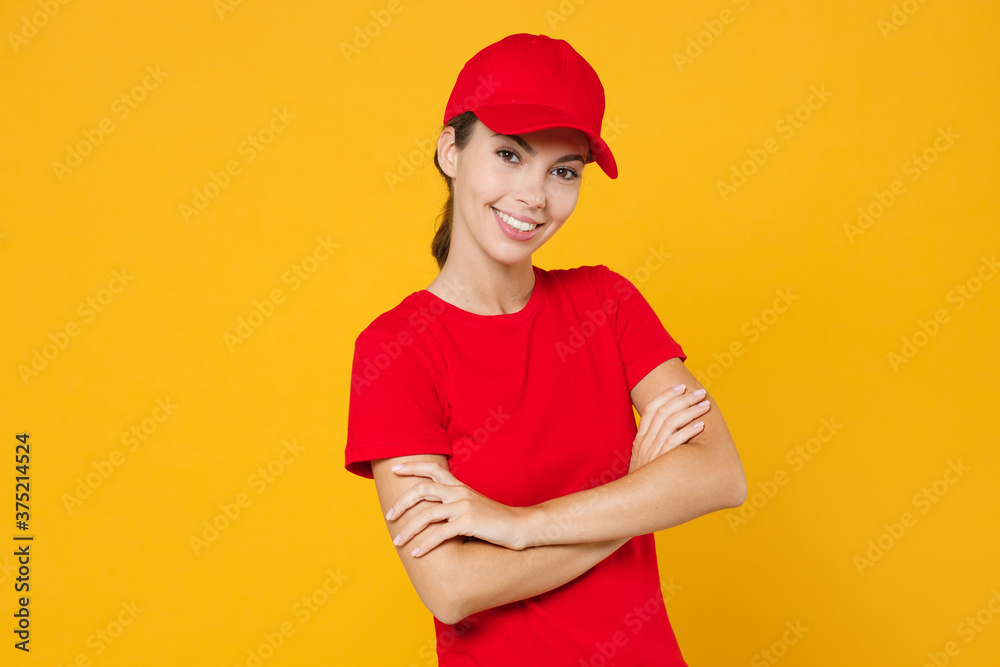 Delivery employee woman in red cap blank t-shirt uniform workwear work courier in service during quarantine coronavirus covid-19 virus, posing look camera isolated on yellow background studio portrait