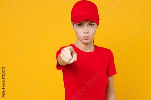 Strict delivery employee woman in red cap blank t-shirt uniform workwear work courier in service during quarantine coronavirus covid-19 virus, look camera isolated on yellow background studio portrait © ViDi Studio