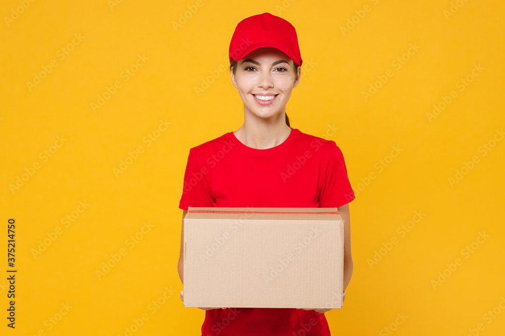 Delivery employee woman in red cap blank t-shirt uniform work courier in service during quarantine coronavirus covid-19 virus holding giving cardboard box isolated on yellow background studio portrait Delivery employee woman in red cap blank t-shirt uniform work courier in service during quarantine coronavirus covid-19 virus holding giving cardboard box isolated on yellow background studio portrait