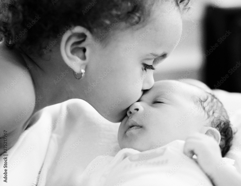 Portrait of a toddler tenderly kissing her newborn sister. Portrait of a toddler tenderly kissing her newborn sister.