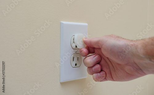 Installing electrical outlet electricity safety cover to prevent child electrocution. Child proofing household power sockets with plastic plug inserts. photo