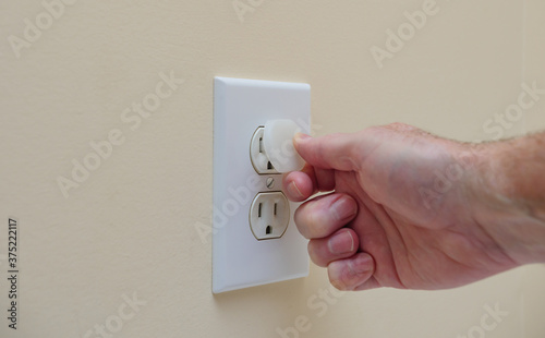 Installing electrical outlet electricity safety cover to prevent child electrocution. Child proofing household power sockets with plastic plug inserts.