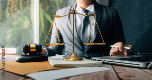 Justice and law concept.Male judge in a courtroom with the gavel, working with, computer and docking keyboard, eyeglasses, on table in morning light