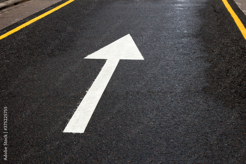 Arrow sign on the road. White arrow on the asphalt. White forward arrow on a blurry street background