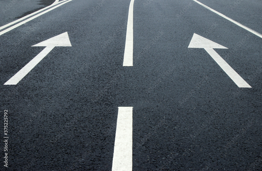 Two arrow signs on the road. White arrows on the asphalt. White forward arrows on a blurry street background Two arrow signs on the road. White arrows on the asphalt. White forward arrows on a blurry street background