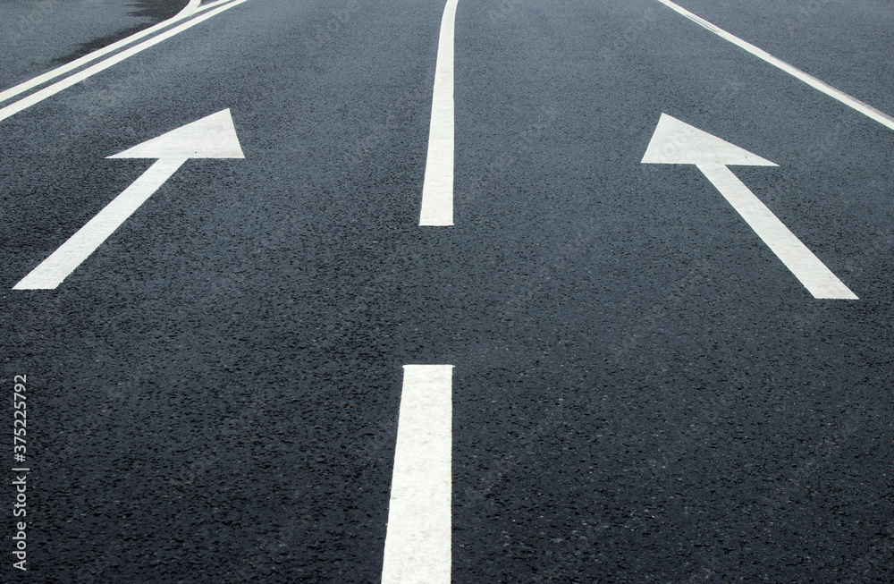 Two arrow signs on the road. White arrows on the asphalt. White forward arrows on a blurry street background