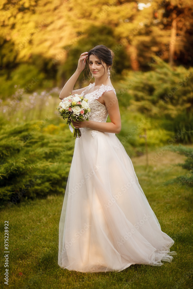 A beautiful bride in a white dress straightening her hair holds a wedding bouquet in her hand. Bride on a walk on a warm autumn day. Portrait of a happy wedding bride on their wedding day