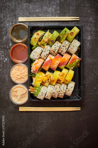 Asian food delivery home, various sushi sets in plastic containers with sauces, rice and chopsticks