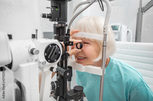 Fototapeta Naklejka Na Ścianę i Meble -  Elderly woman eyesight test with binocular slit-lamp. Checking retina of a female eye close-up. Ophthalmology Clinic