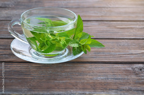 Freshly made hot aromatic mint tea in a glass cup and fresh leaves on a wooden table close-up. Concept of a healthy lifestyle.