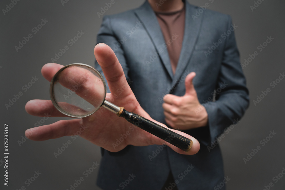 Magnifying glass in the businessman hand close up on gray background. Magnifying glass in the businessman hand close up on gray background.