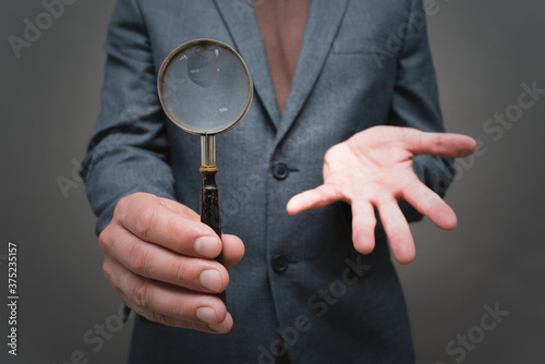 Magnifying glass in the businessman hand close up on gray background.