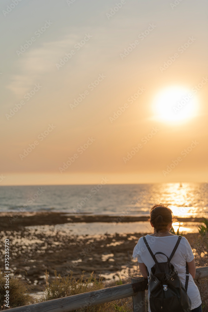 Mujer con mochila mira puesta de sol en la playa