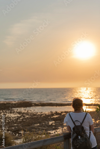 Mujer con mochila mira puesta de sol en la playa
