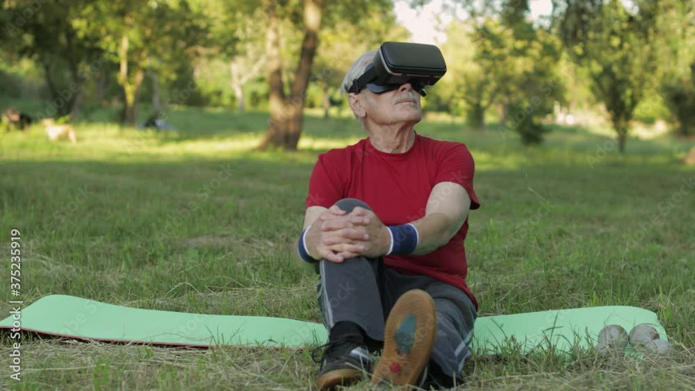Elderly man in VR headset helmet sitting on sport mat. Online sport workout for senior people Elderly man in VR headset helmet sitting on sport mat. Online sport workout for senior people