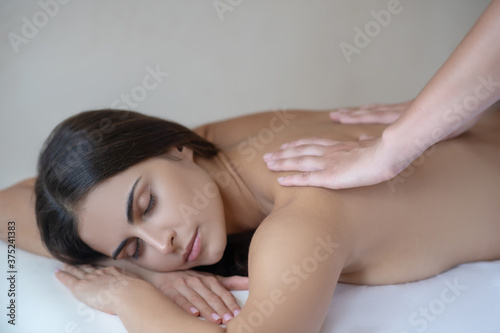 Dark-haired woman having back massage and feeling relaxed