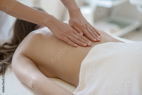 Massage therapist gently rubbing young womans back