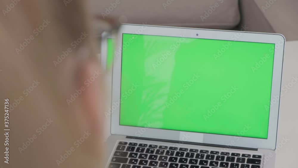 Close up laptop on table with blank green screen, white table. The girl sits with her back and looks into the laptop monitor. Close up laptop on table with blank green screen, white table. The girl sits with her back and looks into the laptop monitor.