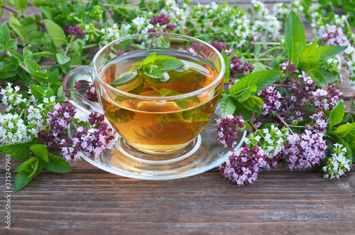 Cup of freshly made hot herbal tea with mint and oregano on a old wooden table. Concept of a healthy lifestyle. photo