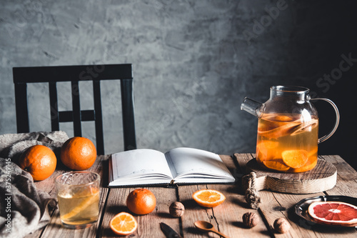 Citrus tea in a transparent teapot with grapefruit and lemon on a wooden table. A book, cooking. photo