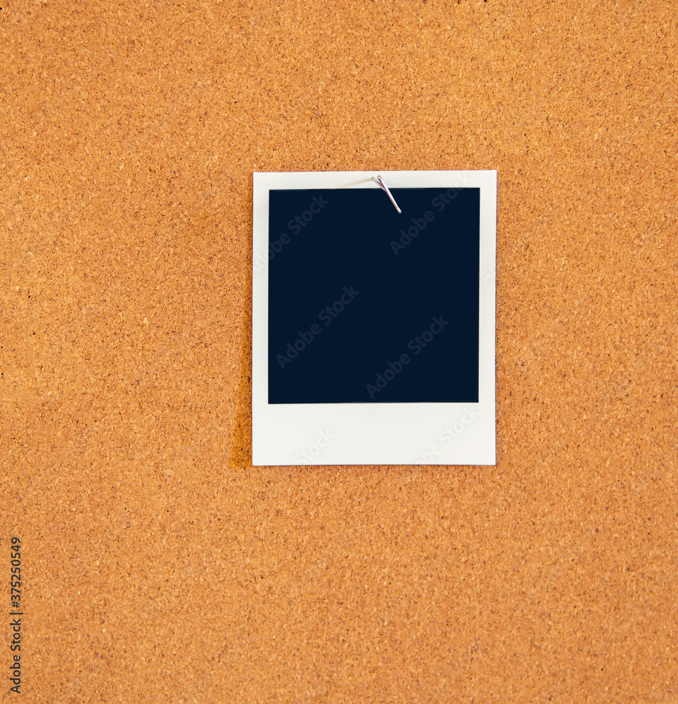 Fototapeta premium A Blank square instant picture pinned to a corkboard with a metal t-pin pushpin.