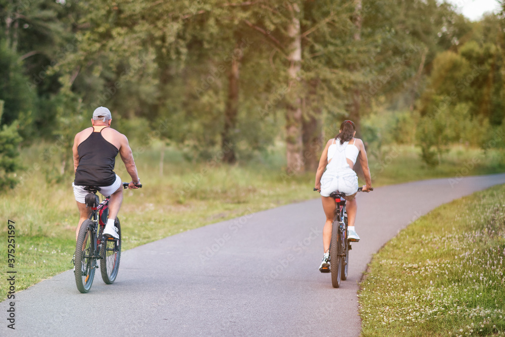 A man and a girl riding their bicycles in a park in summer in the sunny morning.