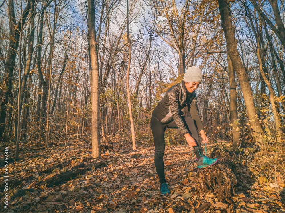 Autumn fall outdoor training running athlete woman on trail run getting ready jogging tying shoe laces outside forest workout wearing warm clothing gloves, winter tights , shoes, jacket. Autumn fall outdoor training running athlete woman on trail run getting ready jogging tying shoe laces outside forest workout wearing warm clothing gloves, winter tights , shoes, jacket.