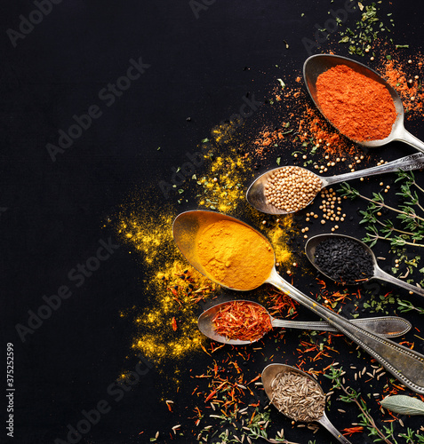 Various spices and herbs on spoons on a black background with copy space