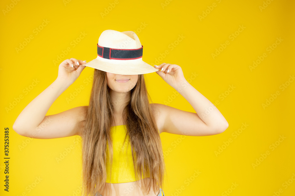 Beautiful girl posing with straw hat on yellow background Beautiful girl posing with straw hat on yellow background