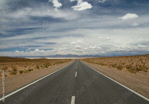Traveling along the empty desert road. Asphalt highway across the arid valley and mountains under a beautiful sky. 