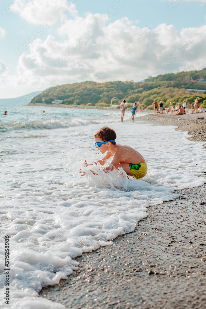 A little boy sits near the sea in foam from the running wave
