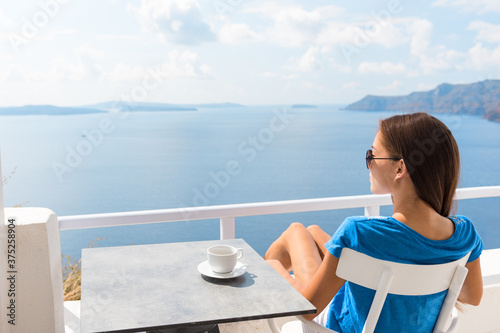 Woman relaxing on hotel balcony enjoying sea view drinking coffee cup during morning breakfast. Luxury resort travel holiday lifestyle girl sitting at table.