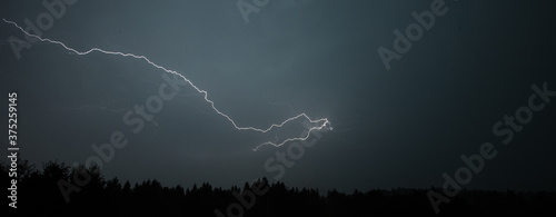 A small horizontal lightning with a skyline of trees or a forest visible below.