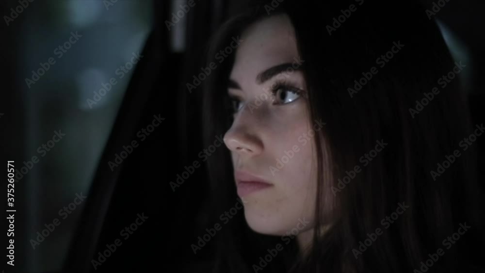 A beautiful young girl sits at the car window against the background of blurry flashing lights of the evening city. Close-up. Side view A beautiful young girl sits at the car window against the background of blurry flashing lights of the evening city. Close-up. Side view