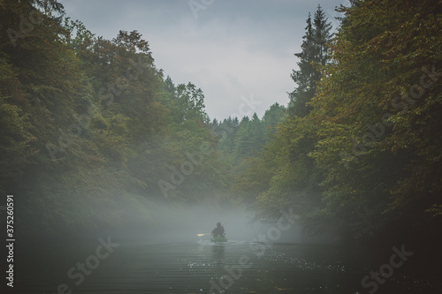 Back view of a green canoe in a misty and foggy river between the trees. Scary spooky and mistery exploration with a canoe on a river Krupa in Slovenia. photo