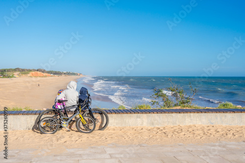 Back view of family looking at the beach, tourists use bicycles. Sunny blue sky outdoors background. Ecotourism activity concept.