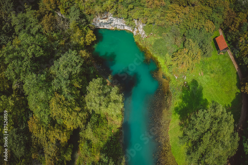 Aerial drone view of river source or spring of Krupa in Bela Krajina (White Carniola) in Slovenia on a misty cloudy day. Visible leaves and foggy green river with rock formation in the back.