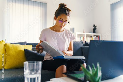 Female girl reading big book learning for academy or school exam - Woman at home on the sofa couch preparing test study in summer day - education concept real people photo