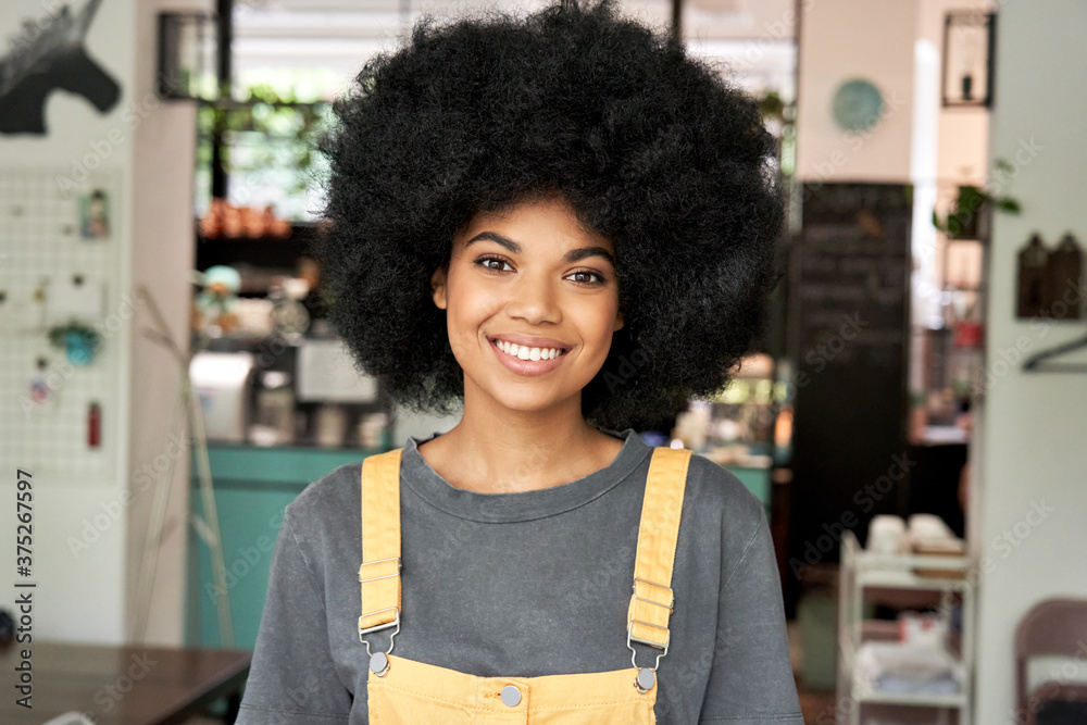 Φωτογραφία Happy stylish African American gen z hipster female student with Afro hair looks at camera stands in cozy cafe interior
