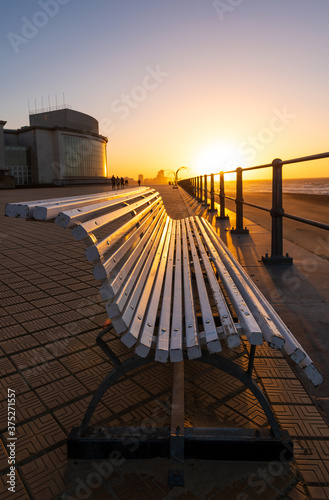 Sunset along the waterfront promenade with a bench in the foreground in Oostende  Ostend  by its North Sea beach with a skyline view in the background  Belgium.