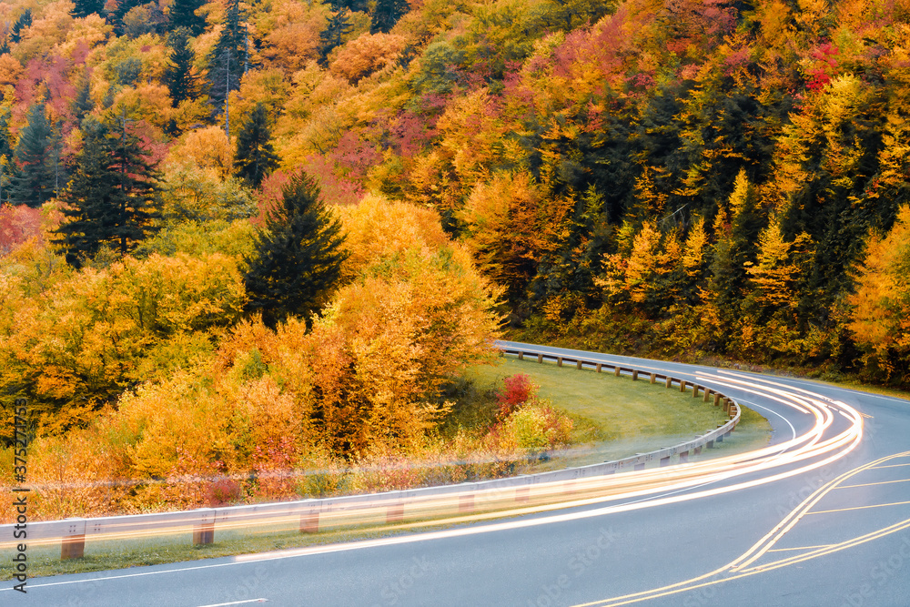 Fototapeta premium Blurred car lights on a mountain road against a colorful Autumn scene.